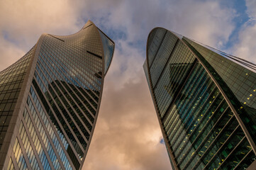 Skyscrapers in business district against blue sky. Looking Up high-rise office buildings. Evening time, sunset. Orange, yellow and gold shades of color. Angled view.