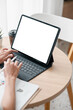 © Satori Studio - Hands typing on a tablet with a blank screen in a bright workspace, featuring coffee and documents on a wooden table.