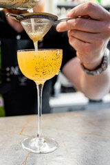 Wall Mural - A close-up of a hand pouring a vibrant, bubbly orange drink through a strainer into an elegant stemmed glass, focusing on the drink’s texture and the action of pouring. Perfect for cocktail themes.