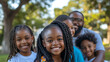 © Tobi - Multi-generational family smiling and posing in a park setting, kids in front and adults behind, enjoying a sunny day