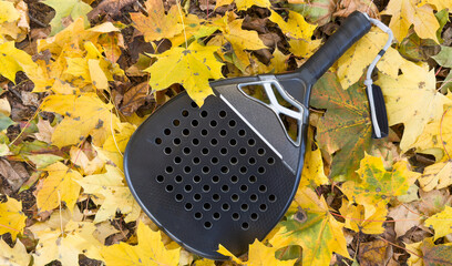 Top view of a black padel racket on a green court grass turf behind the net outdoors. Paddle is a racquet game. Professional sport concept with space for text