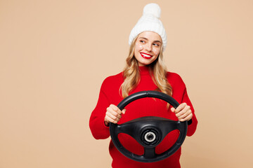 Canvas Print - Merry young minded fun woman wear red warm cozy sweater hat posing hold steering wheel driving car look aside isolated on plain beige background. Happy New Year celebration Christmas holiday concept.