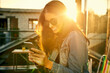 © peopleimages.com - Woman, sunglasses and outdoor with phone for typing, sun flare and app for communication on holiday. Female person, travel and city for vacation in Madrid, surfing social media and search online