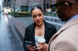 © bernardbodo - Businesswoman holding coffee and smart phone listening to businessman in new york city