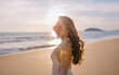 © YiuCheung - A woman in sunglasses smiles at the sunset while walking on a sandy beach.