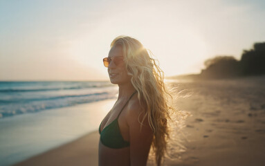 A young woman with long blonde hair and sunglasses stands on a sandy beach, the ocean waves gently lapping at the shore behind her. The golden light of the setting sun illuminates her, creating a warm