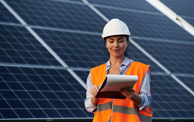 Notepad in hands. Female worker engineer in uniform is near solar panels