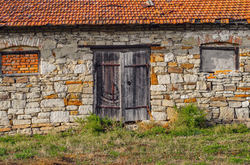 Old stone barn with weathered wooden doors, red tile roof, rustic countryside architecture, vintage farm storage, history and decay in rural setting