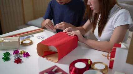 Wall Mural -  cheerful couple wrapping gifts together at a decorated table with a Christmas tree in the background, capturing the festive holiday spirit. The man takes a selfie to remember the moment