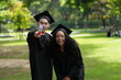 © ultramansk - Two graduates in caps and gowns joyfully celebrate, each holding a diploma with smiles and raised hands. Their excitement shines in an outdoor park with greenery, marking a proud moment of achievement