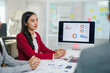 ©  NCST Studio - Businesswoman leading a meeting, discussing charts and graphs displayed on a computer screen with colleagues in a modern office
