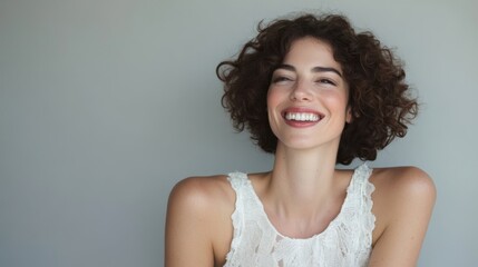 A young woman with curly hair smiles warmly while wearing a casual top