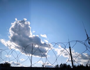 Barbed wire on a summer day against a peaceful sky with clouds and rays of the sun