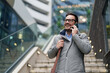 © Dorde - A cheerful mid-adult Caucasian man in professional attire talks on his smartphone against an urban backdrop, steps leading to a building visible behind him.