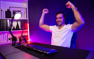 Winner of smart streamer playing online game wearing headphones raising fist up on streaming gamer with social media. Esport skill team player online digital gaming at neon light studio room. Surmise.