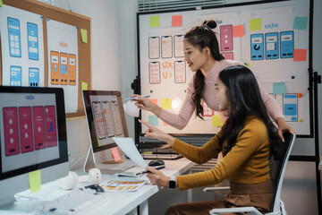 Two female web designers working together developing wireframe for mobile application on desktop computer in the office