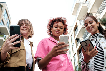 three young women are using mobile phones while walking in the city