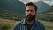 © Thanapol - Man with a beard stands in a green valley surrounded by mountains under a partly cloudy sky during daylight hours