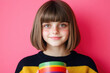 © Konstiantyn Zapylaie - Smiling young girl with freckles holding colorful rainbow cup against pink background