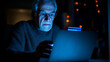 © Maksym - An elderly man, bathed in the cool glow of a laptop screen, holds his credit card and browses online shopping websites, the scene symbolizing his vulnerability to fraudulent scheme