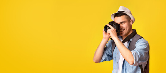 Active traveler happy young guy taking photos, using camera over orange background, panorama with copy space