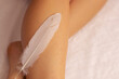 © Alina - A person gently touches a soft feather against their leg in a serene indoor setting
