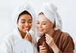 © Prostock-studio - Joyful international girlfriends in bathrobes putting lipsticks, looking at mirror