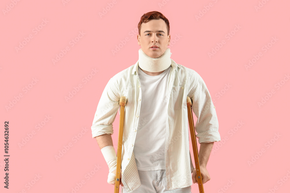 Injured young man after accident with crutches on pink background