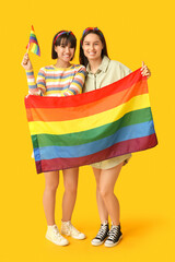 Wall Mural - Young lesbian couple with LGBT flags on yellow background