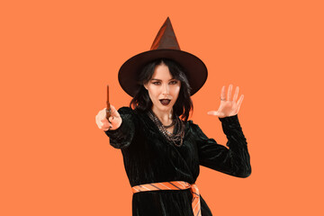 Beautiful young woman dressed as witch for Halloween with magic wand on orange background