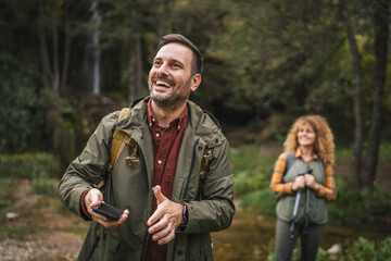 Adult man hiker use mobile phone while his wife stand behind him