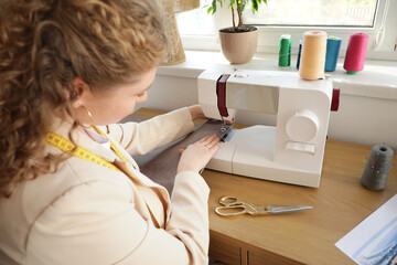 Wall Mural - Female fashion designer sewing clothes at table in studio, closeup