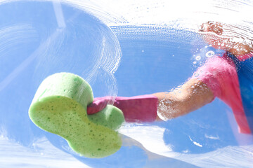 Woman washing window with sponge against blue sky, closeup