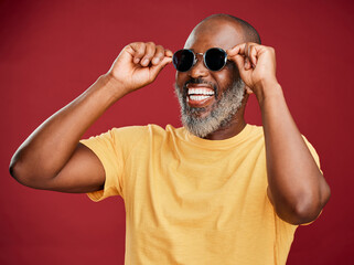 Wall Mural - Black man, fashion and laughing with sunglasses in studio for trendy style, designer eyewear or summer ready. Mature person, happy or edgy face accessory for aesthetic or confidence on red background