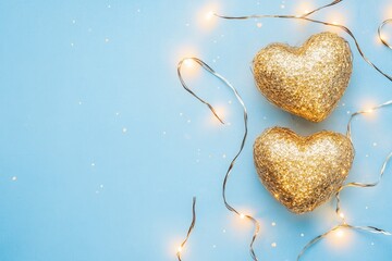 Two golden hearts with luminous garland on light blue background. Selective focus. Valentines day card. Closeup. Valentine's day concept. Banner. with generative ai