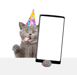 Poster - Happy kitten with tongue out wearing party cap shows big smartphone with blank screen above empty white banner. Empty space for text. isolated on white background