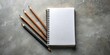 © Triple P - A blank notebook with three pencils placed in a diagonal formation on a textured surface, ready for creative endeavors.