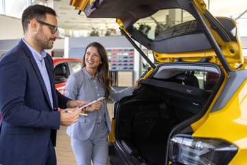 Super sales team in dealership, two consultants or managers in elegant suits with laptop and tablet in arms in car dealership