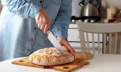 Close-up of female hands cutting fresh homemade bread at home in the kitchen.