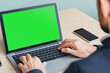 © Vasili - A person's hand using a laptop with a green screen in a modern office setup. Ideal for mockups and copy space for tech-related content.