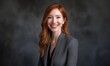 © Krisartist94 - Professional young woman with long red hair poses confidently in a gray suit against a dark background during a business portrait session