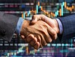 © Metthaisonk - Close-up of a handshake between two professionals in front of a stock market graph, symbolizing a successful business agreement.