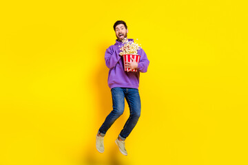 Full length photo of nice young male jump eat popcorn dressed stylish violet garment isolated on yellow color background