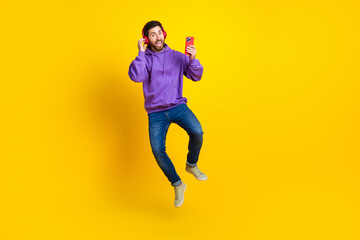 Full length photo of nice young male dance jump headphones device dressed stylish violet garment isolated on yellow color background