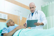 © Thirawatana - Doctor discuss to a patient in the hospital. Specialist male doctor describing the improving symptoms of elderly patient.