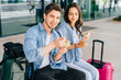 © Iryna - Caucasian man and woman casually dressed engaged in conversation. Couple travelers with luggage eating snacks at airport terminal outdoor.