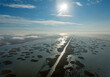 © AmazingAerialAgency - Aerial view of tranquil wetlands with a winding road and serene river under a bright sky, Astrakhan Nature Reserve, Russia.