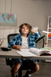 © Guys Who Shoot - in the children's room a schoolboy in a white sweater and a blue checkered shirt at a desk doing homework on his studies writing in notebook looking up thinking