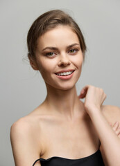 Poster - Smiling young woman with natural beauty, wearing a black strapless top. Soft gray background highlights her features. Radiating confidence and joy.