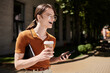 © Bliss - A joyful non binary individual carries a coffee cup and phone while strolling down a sunny path.